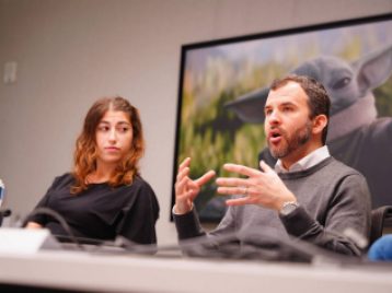 ESPN and Disney employees giving a talk, sitting behind a table, with a Mandalorian image behind them on the wall. 